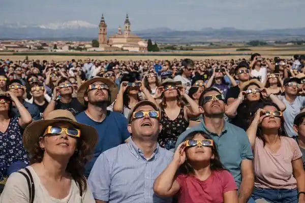 Crowd wearing eclipse glasses watching a solar eclipse in Spain with church landscape in the background.